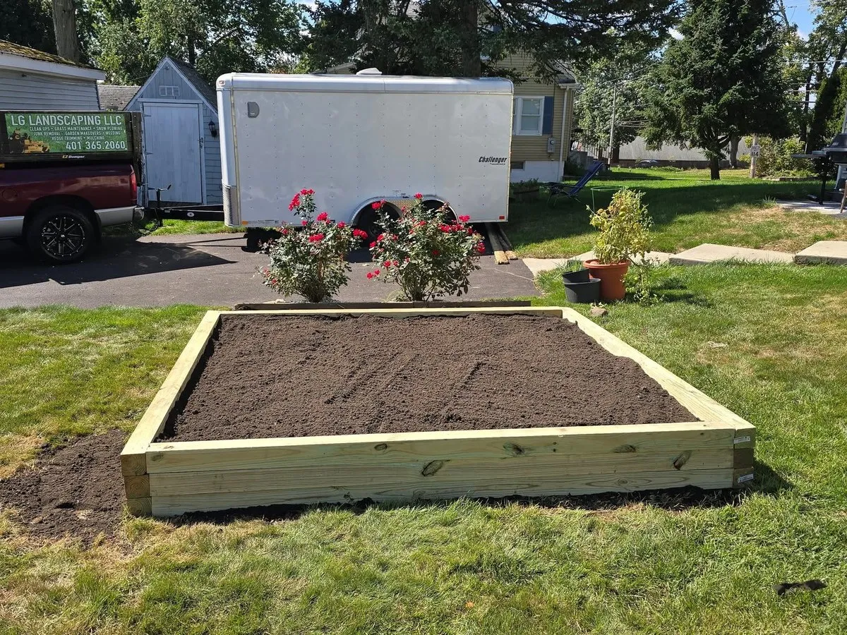 Newly built timber raised garden bed filled with soil, with rose bushes and the LG Landscaping truck and trailer behind