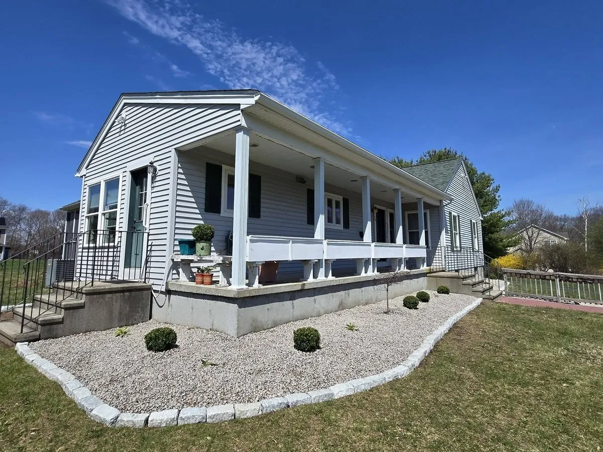Gray stone bed with granite cobblestone edging and boxwood shrubs along the foundation of a white porch-front house